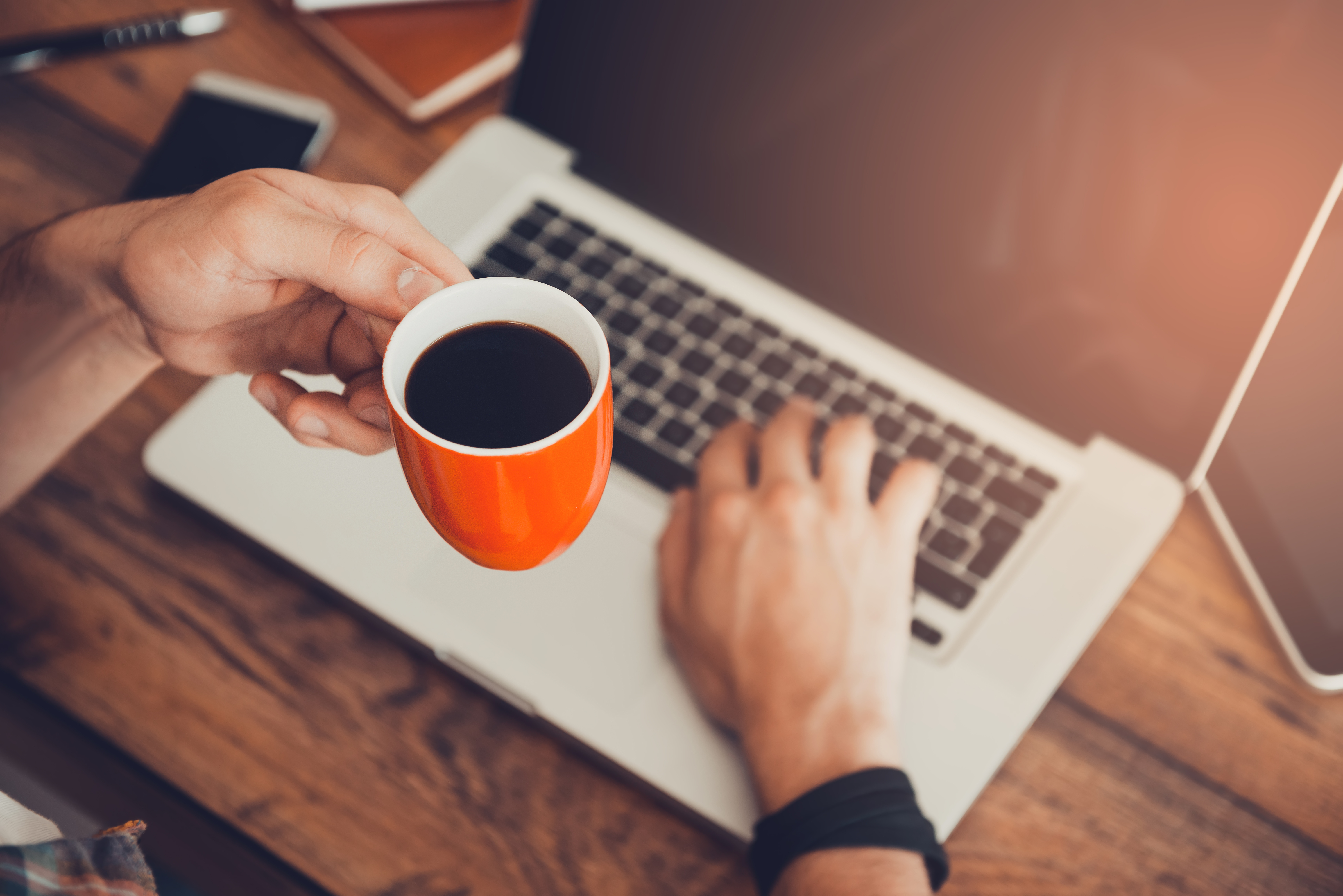 Man working on laptop and holding cup of coffee